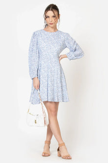 Woman in a light blue floral long sleeve dress with white handbag and beige sandals
