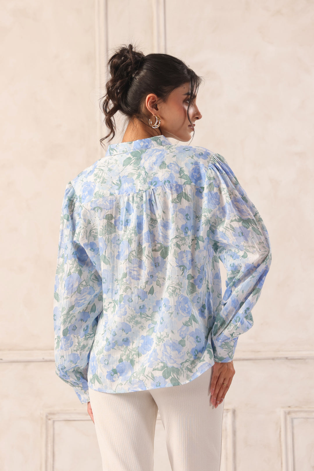 Woman wearing blue floral print blouse with puff sleeves, back view, paired with white pants for Western wear style