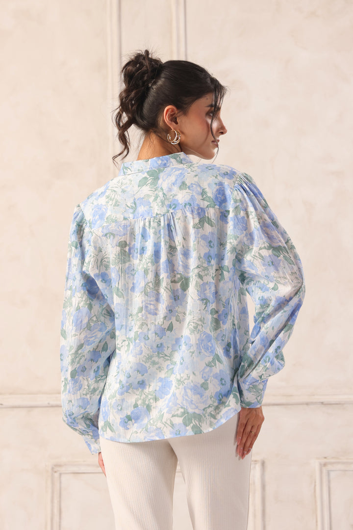 Woman wearing blue floral print blouse with puff sleeves, back view, paired with white pants for Western wear style