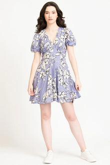Woman wearing a lilac floral print mini dress with short puff sleeves and white sneakers