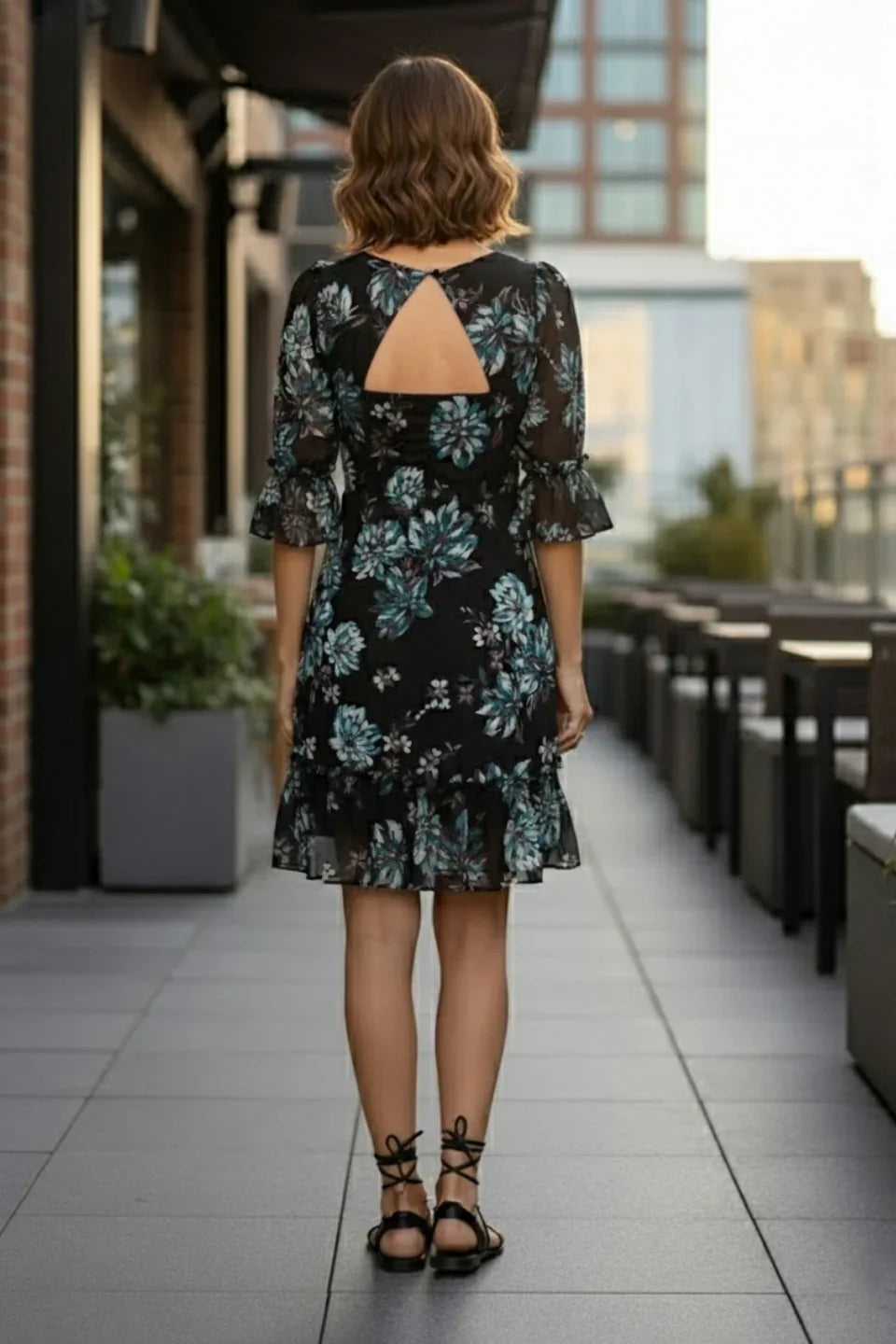 Woman in black floral print dress with open back and ruffle hem on outdoor terrace
