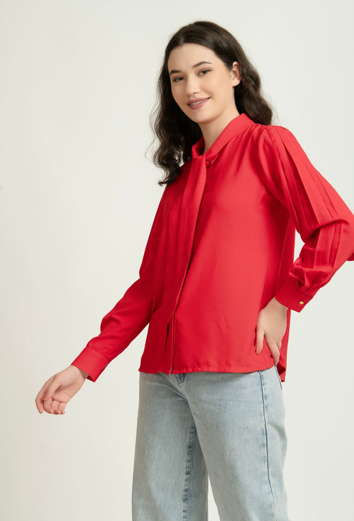 Woman wearing red Western-style blouse with tie neck and puffed sleeves, paired with light jeans