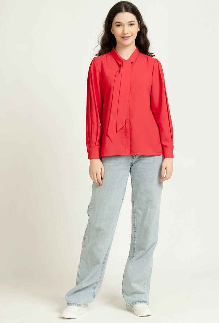 Woman wearing red tie-neck blouse with long sleeves, paired with light wash wide-leg jeans and white sneakers