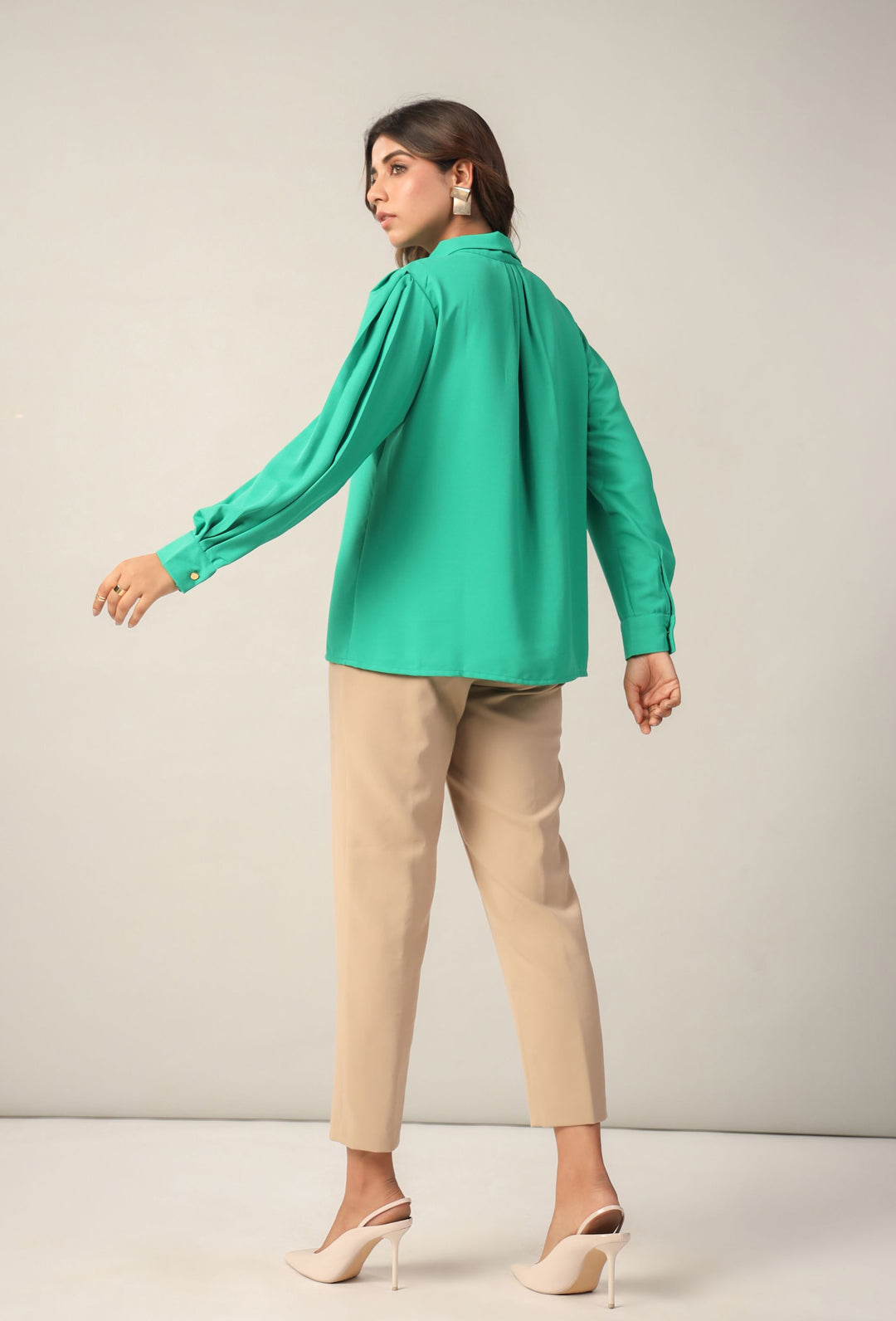 Woman in emerald green blouse with puff sleeves, beige pants, and white heels — chic Western wear outfit