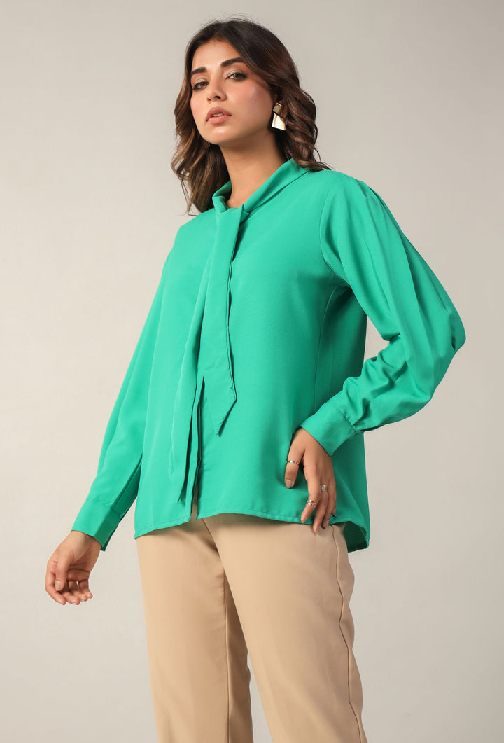 Woman in emerald green long sleeve blouse with tie neck, paired with beige pants for chic Western wear