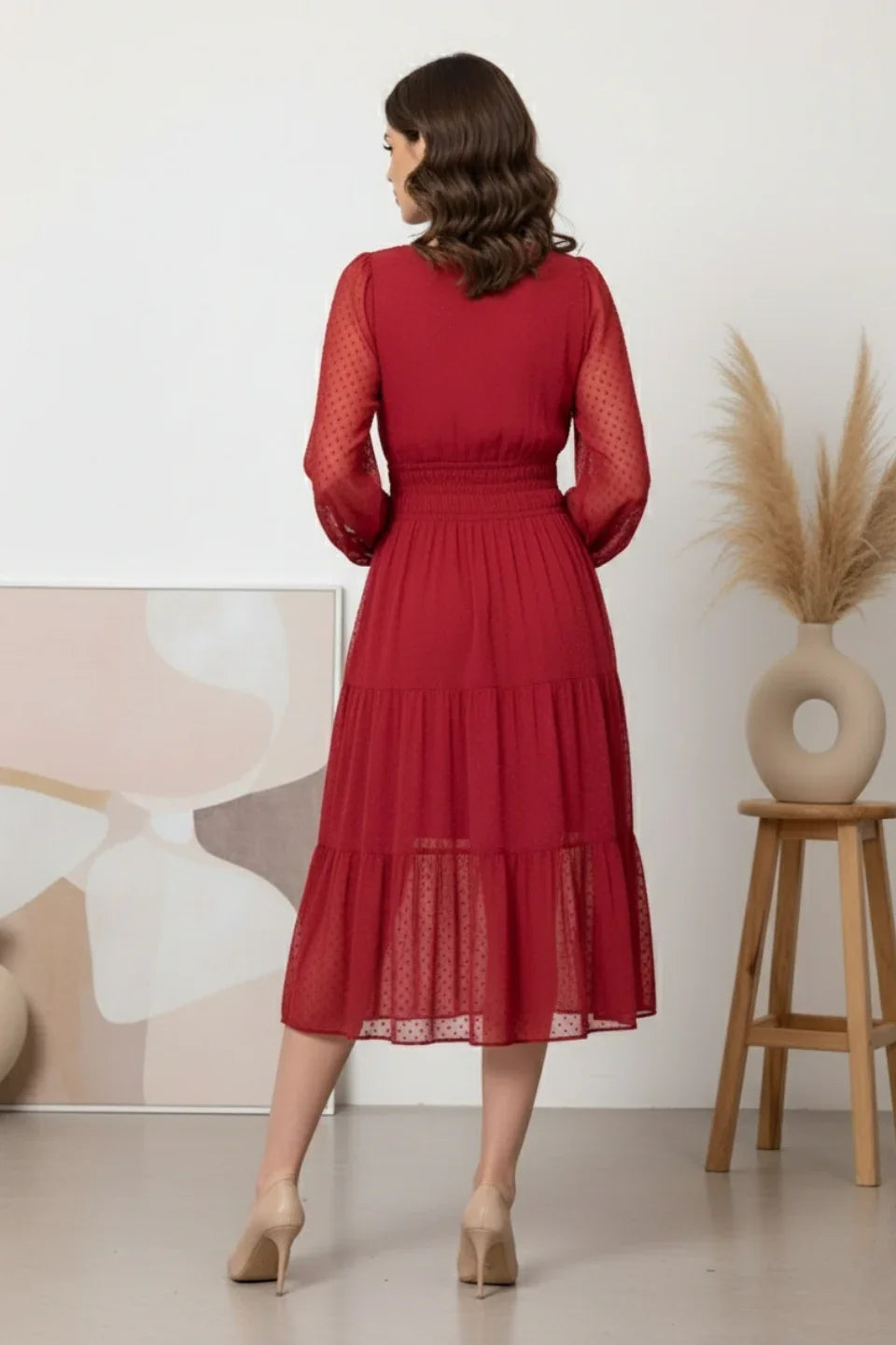 Woman in a red long-sleeve midi dress with sheer dotted sleeves and tiered skirt standing indoors