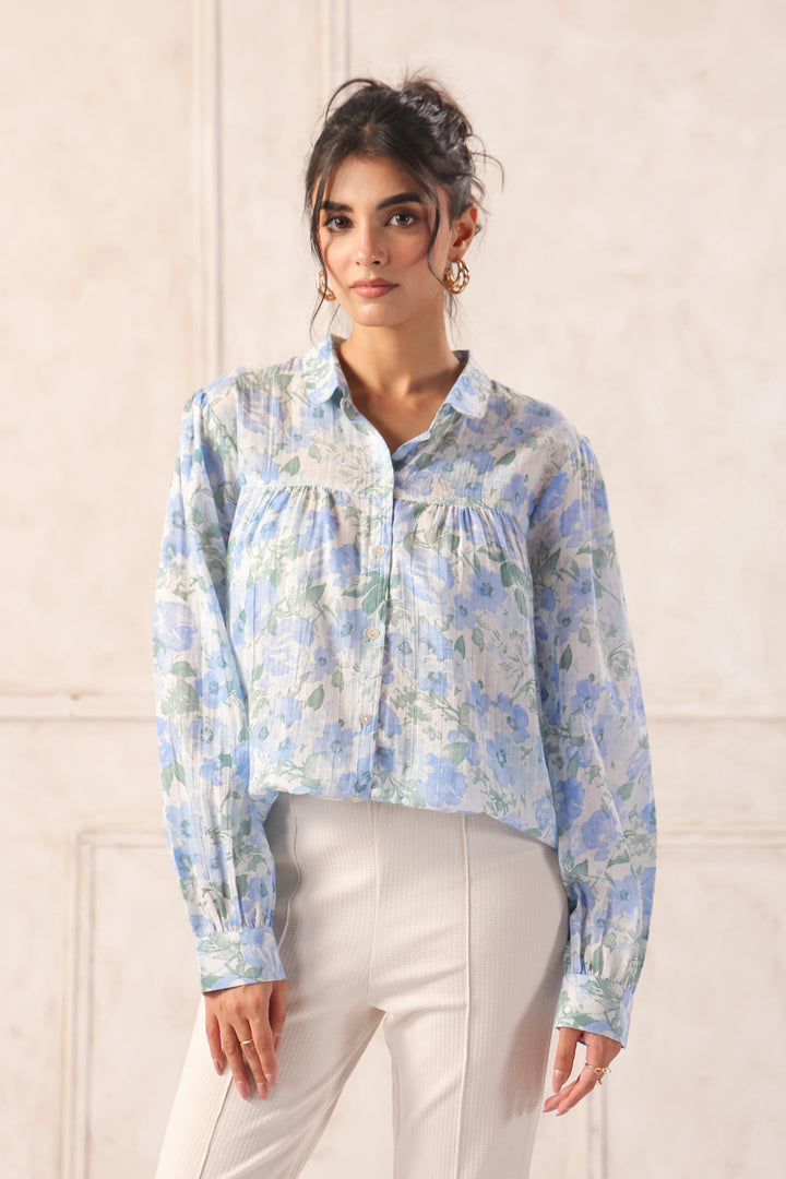 Blue floral print button-up shirt with ruffled details, paired with cream trousers for a chic Western wear look.
