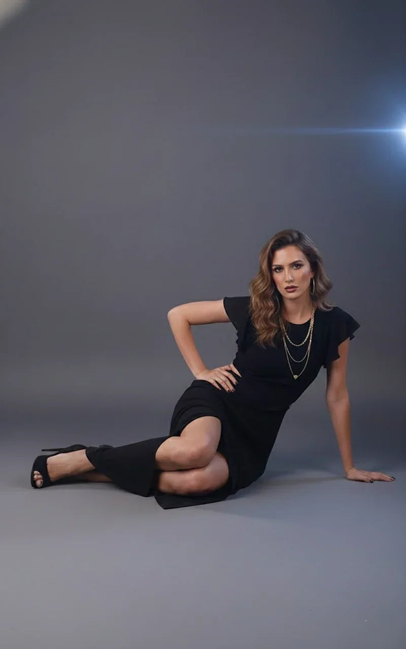 Woman in black maxi dress with short sleeves sitting on floor, wearing layered gold necklaces