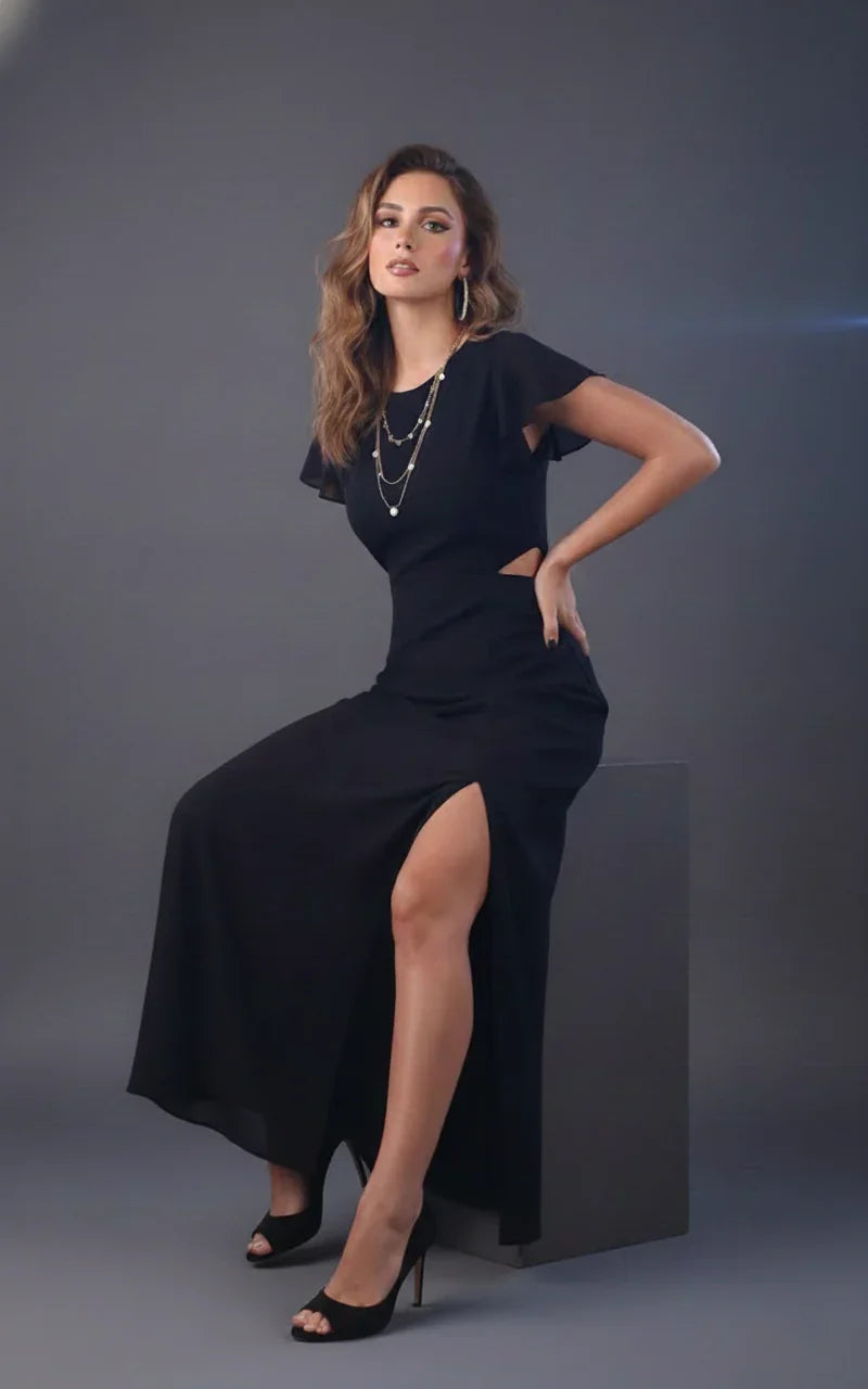 Woman in elegant black maxi dress with side cutouts and thigh-high slit, posing in studio