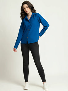 Woman wearing bright blue long sleeve shirt with black skinny jeans and white sneakers