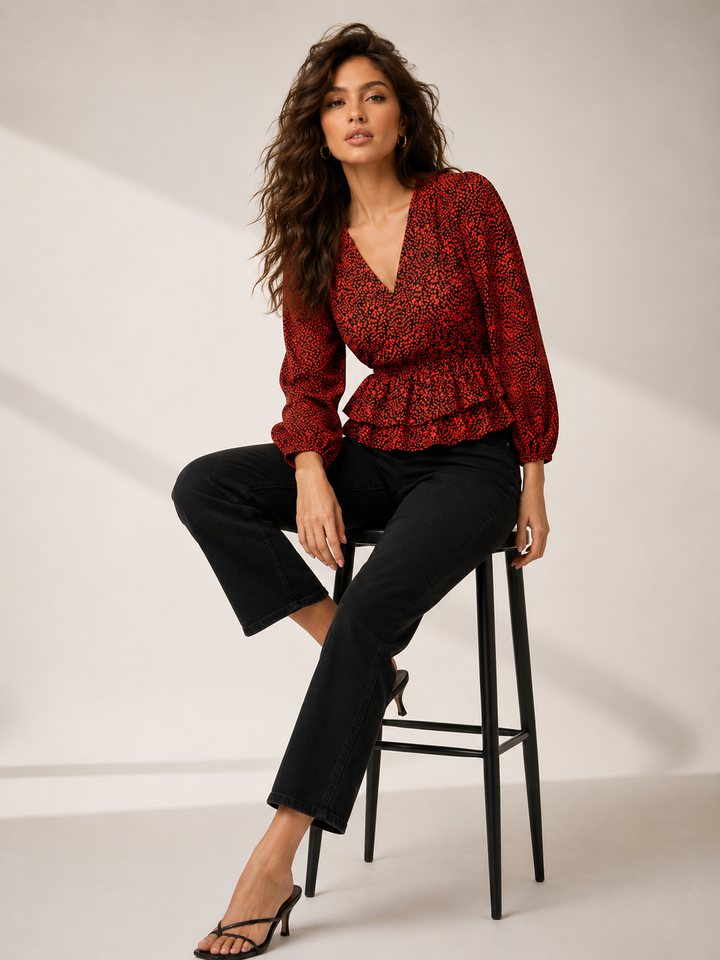 Woman in red floral wrap top with ruffle hem, black jeans, and heels, seated on stool