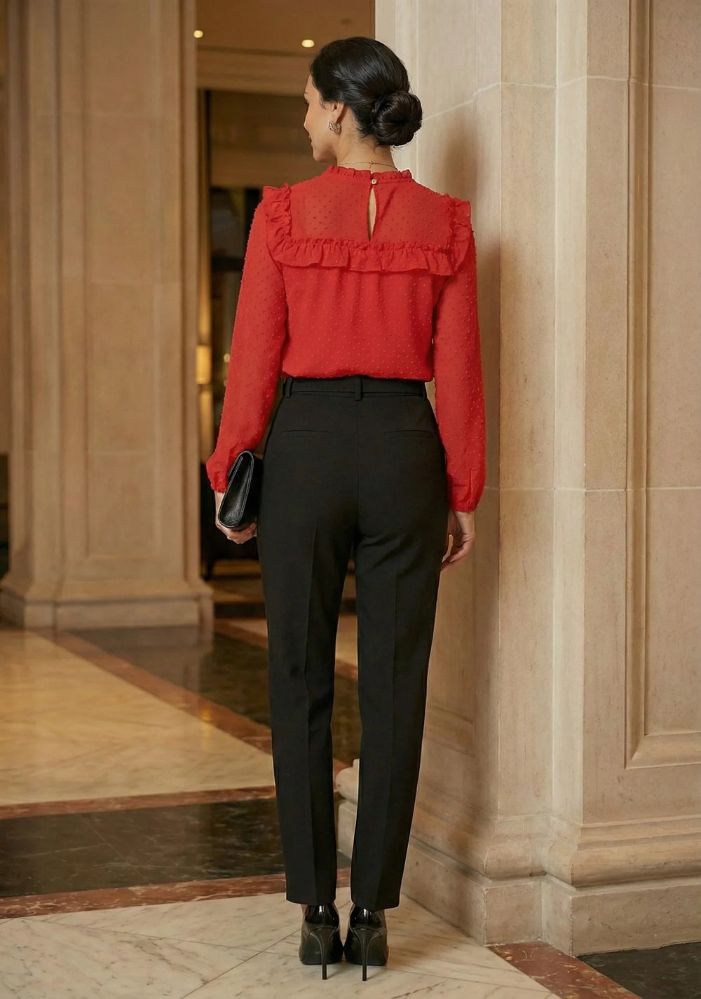 Woman in red ruffle chiffon top and black pants standing indoors, back view