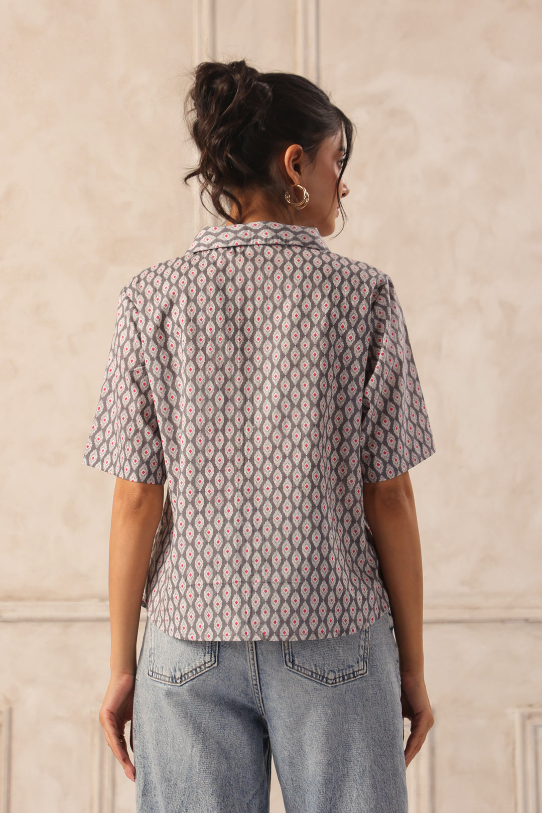 Woman wearing gray geometric print Western shirt with short sleeves, paired with blue jeans, back view.