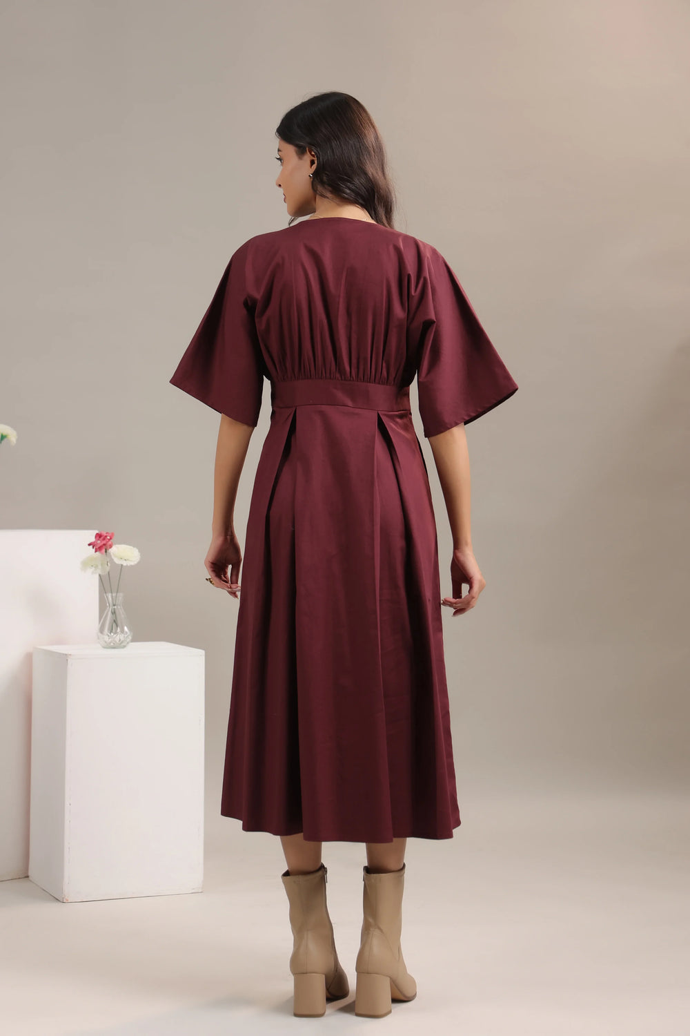 Woman modeling maroon midi dress with flared sleeves and tan boots, back view