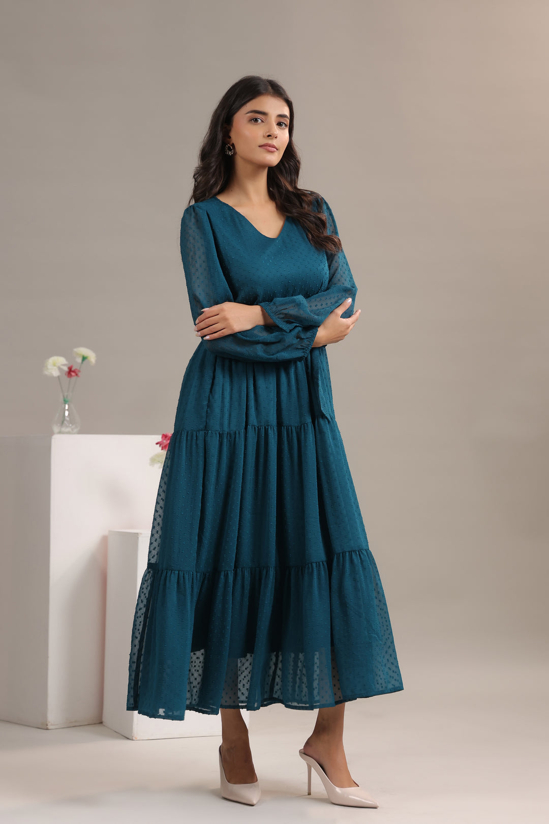 Woman wearing a teal dress standing against a neutral background