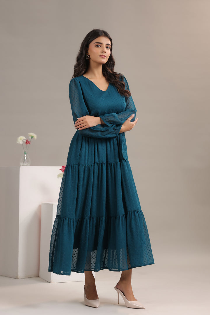 Woman wearing a teal dress standing against a neutral background