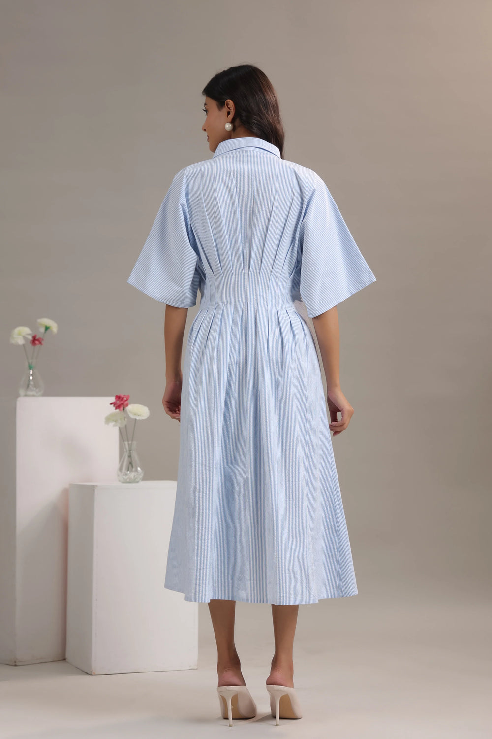 Woman in light blue pinstripe midi dress with flared sleeves, styled with heels