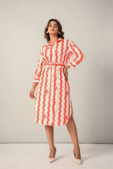 Woman in a red and white western print shirt dress with belt, standing against a plain background