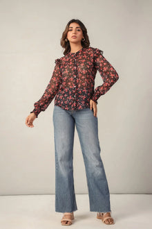 Woman in a sheer floral print blouse with ruffle sleeves and blue flared jeans