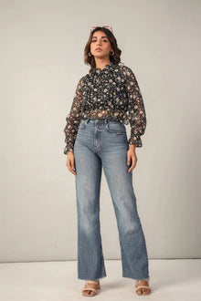 Woman wearing a sheer floral blouse with high-waisted wide-leg jeans and nude heels