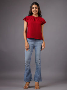 Woman wearing a red short-sleeve top and blue flare jeans, standing against a plain background