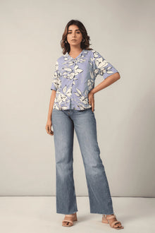 Woman in floral print button-up shirt and wide-leg jeans, standing in studio setting