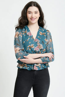Woman wearing teal floral wrap top with three-quarter sleeves and ruffle hem, paired with black jeans.