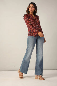 Woman wearing a maroon floral ruffle top with blue flared jeans and beige heels