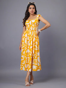 Woman wearing yellow printed midi dress with cap sleeves and white sandals, standing against a grey background