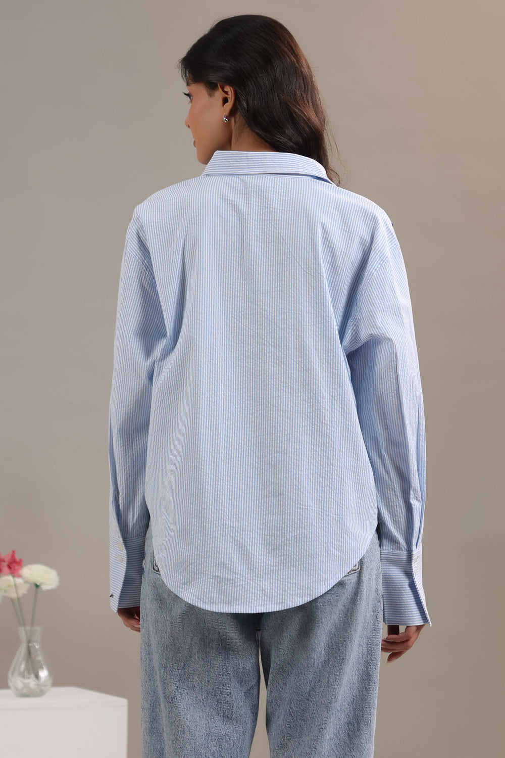 Woman in blue and white striped shirt and denim jeans, back view, neutral background