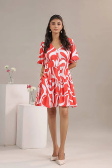 Woman in red and white printed short dress with flared sleeves, posing indoors