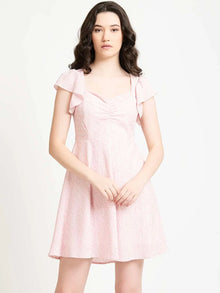 Woman wearing a light pink short dress with flutter sleeves, standing against a white background.