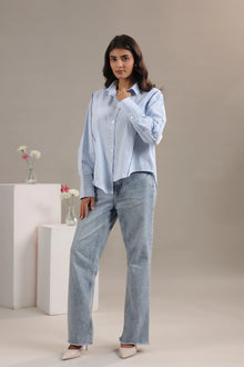 Woman wearing a blue striped shirt and light wash jeans, full body style in studio setting